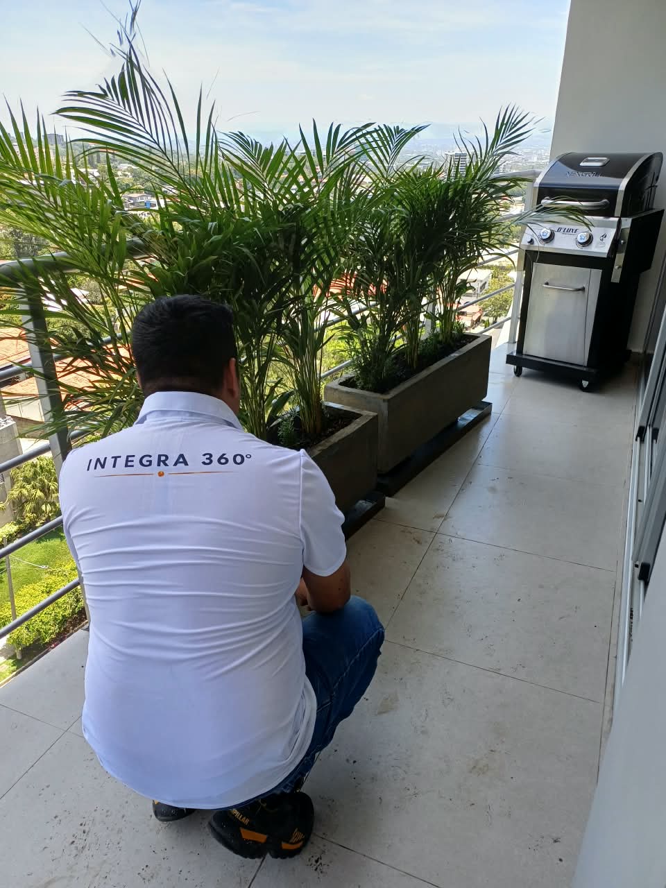 Técnico de INTEGRA 360° realizando mantenimiento de macetas y plantas en terraza residencial con vista a la ciudad